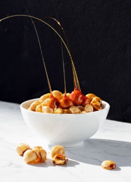 White bowl of candied hazelnuts and hazelnut spikes with a dramatic black and white background.