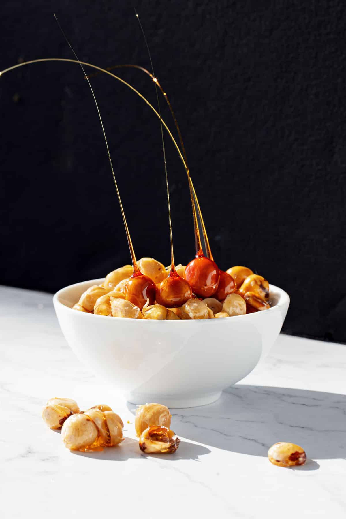 White bowl of candied hazelnuts and hazelnut spikes with a dramatic black and white background.