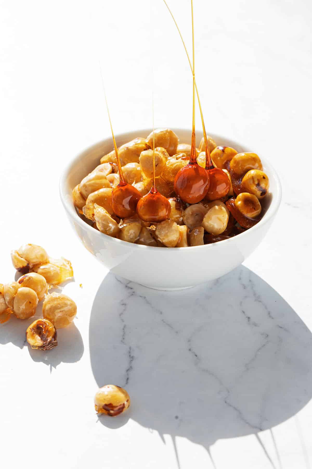 White bowl filled with candied hazelnuts and hazelnut spikes, with a few clusters on the side.