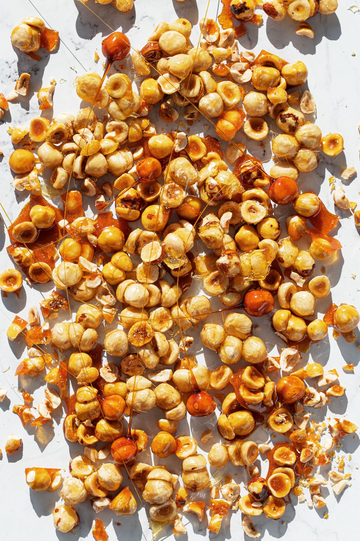 Overhead, messy scattered candied hazelnuts and spikes on a white background.