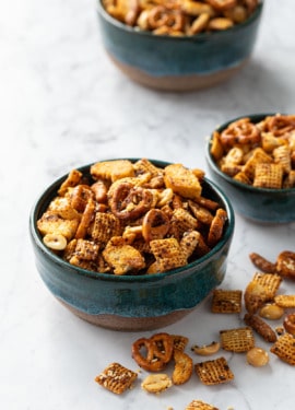 Three teal ceramic bowls overflowing with homemade snack mix on marble background.