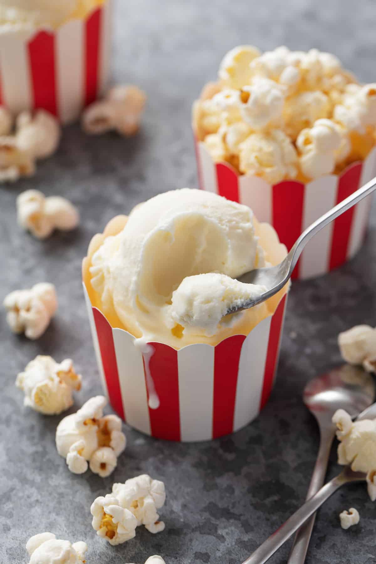 Red and white striped paper cup with a scoop of homemade Buttered Popcorn Ice Cream and silver spoon scooping a spoonful to show the creamy texture.