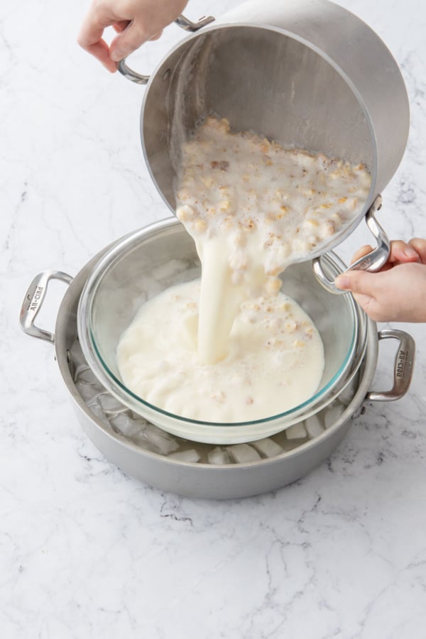 Pouring popcorn ice cream base into a bowl set inside a pot with ice water to cool.