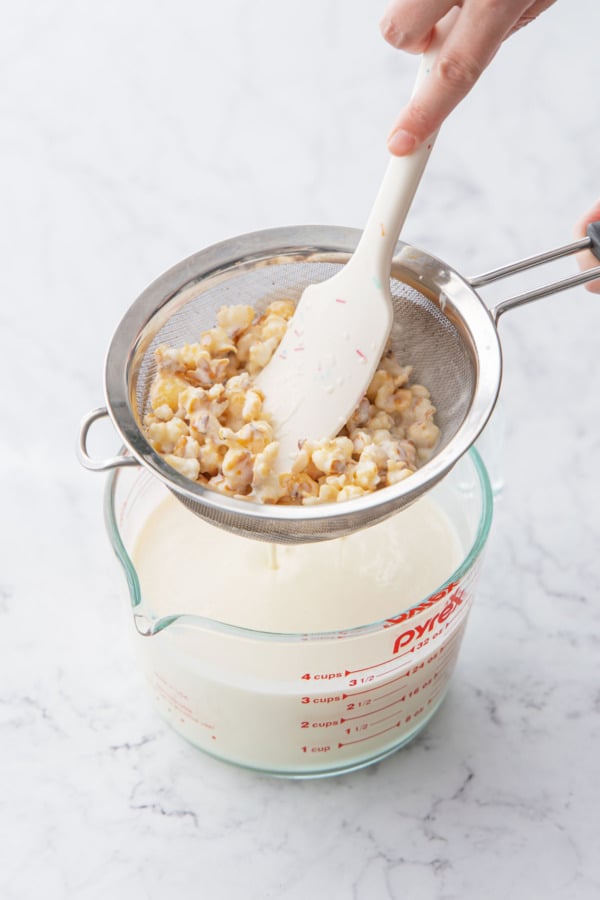 Pressing the popcorn through a sieve to extract as much liquid as possible.