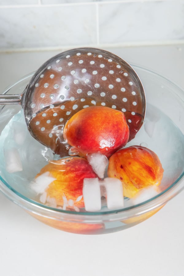 Transferring peaches to an ice water bath after boiling.