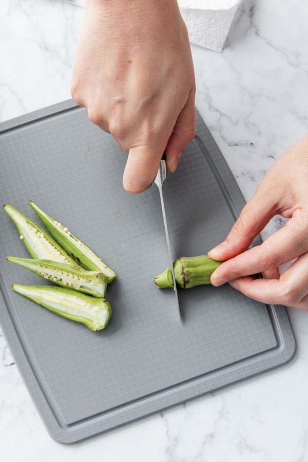 Cutting stem end off of okra pods with a small knife.