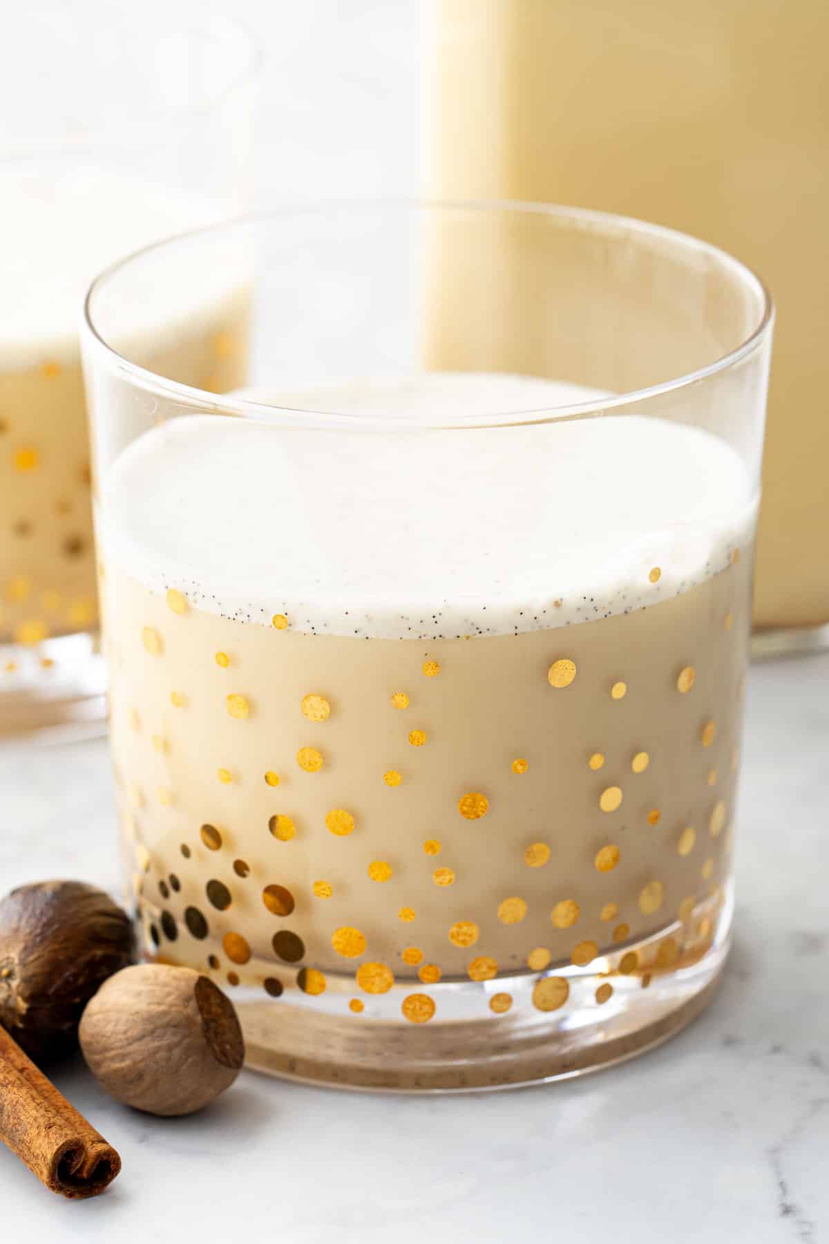 Closeup of a gold polka dot drinking glass filled with homemade eggnog, with a visible layer of vanilla bean-speckled froth on top.