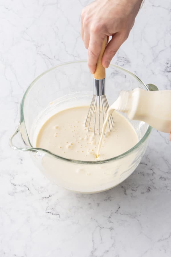 Whisking in heavy cream to homemade eggnog mixture in a mixing bowl.