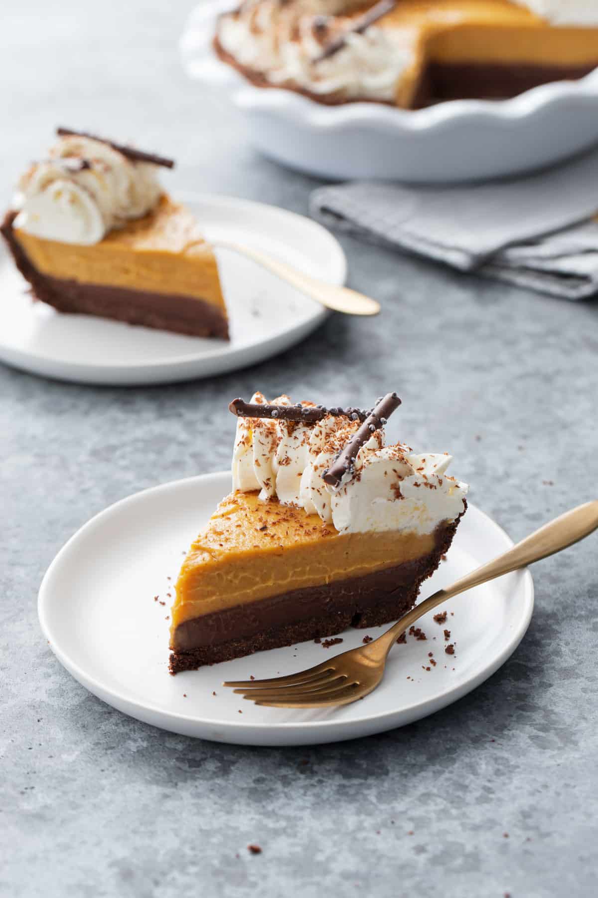 Slice of Black Bottom Pumpkin Cream Pie with a layer of Chocolate Ganache on the bottom, topped with whipped cream and grated chocolate.