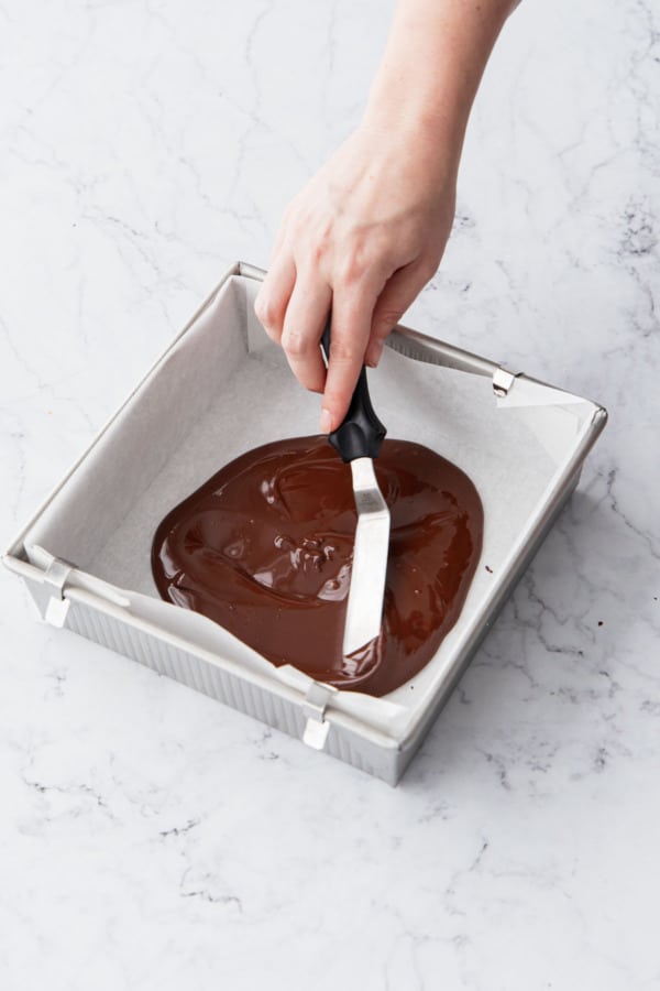 Spreading chocolate out into an even layer in the bottom of a parchment lined pan.