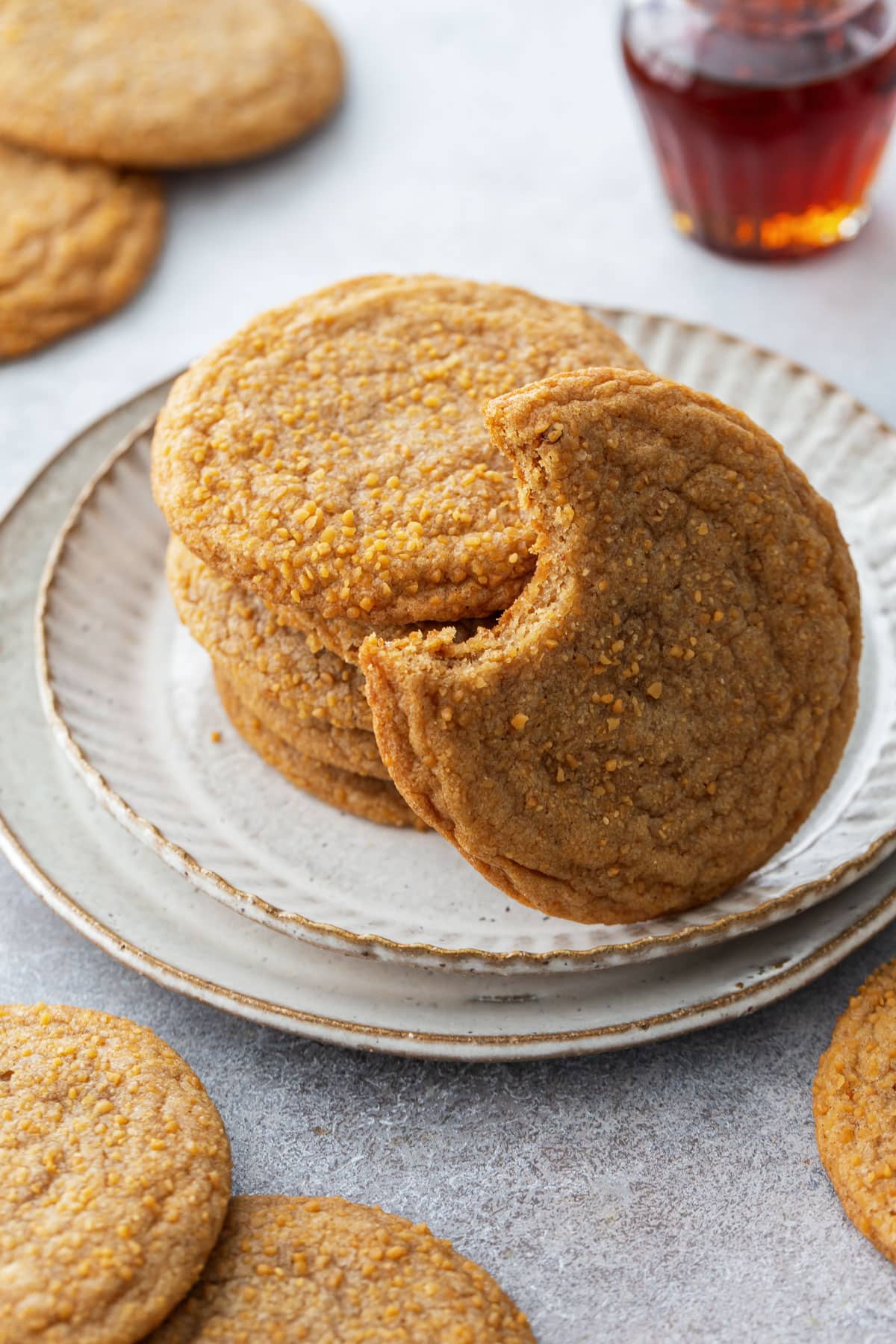 Stack of Maple Brown Butter Sugar Cookies on a plate, one with a bite taken out of it to show the chewy texture.