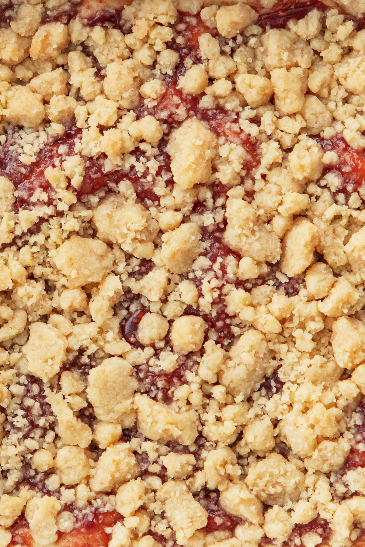Overhead closeup of the crumb top of a Jammy Sour Cream Crumb Cake, with specks of red fruit jam showing through the blonde-colored crumb.
