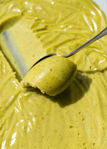 Close up shot of a spoon scooping a curl of bright green pistachio ganache.