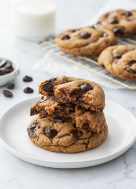 Stack of Brown Butter Chocolate Chip Cookies on a white plate, one cookie split in half to show the gooey interior texture.