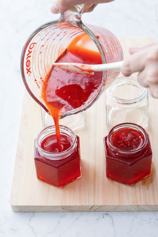Pouring strawberry elderflower jelly into sterilized jars for canning.