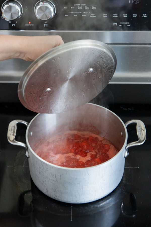 Cooking mashed strawberries with a lid on the stovetop.