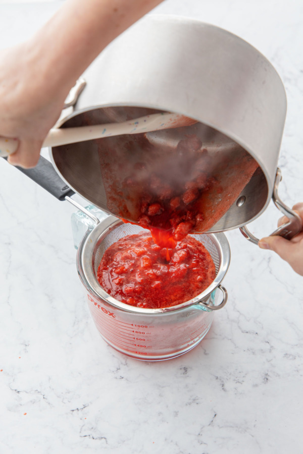 Straining stewed strawberries through a fine mesh sieve.