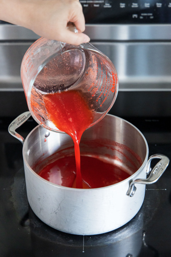 Pouring strawberry juice back into the medium saucepan on the stove.