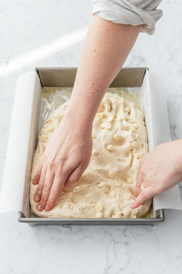 Lightly pressing the focaccia dough into the shape of the baking pan.