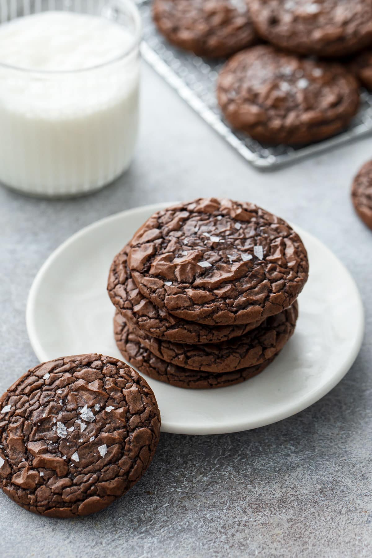 Stack of Chewy Crinkle-Top Brownie Cookies on a plate with one cookie propped on the rim to show the shiny, crackly top texture.