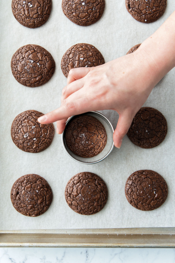 After baking, swirling a round cookie cutter around each still-warm cookie to perfect the round shape.