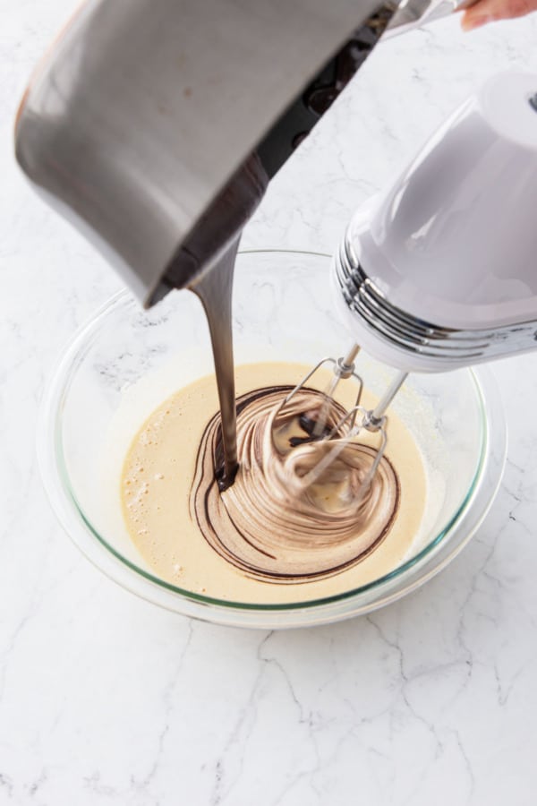 Pouring melted chocolate mixture into the mixing bowl with whipped sugar and eggs.