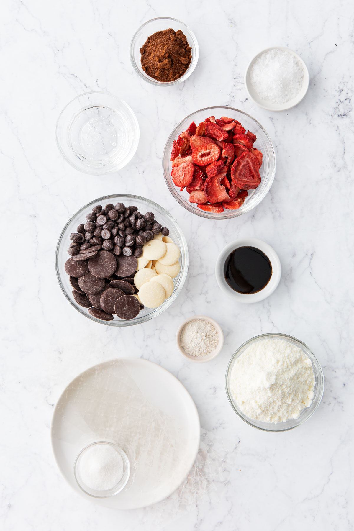 Overhead flatlay on a marble background with bowls of varying sizes filled with different ingredients.