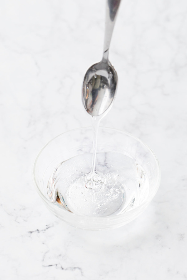 Clear bowl filled with glucose syrup, a spoon drizzling the syrup to show texture and thickness.