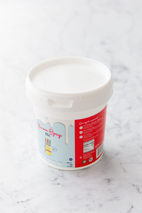 Tub of glucose syrup on a white marble background.
