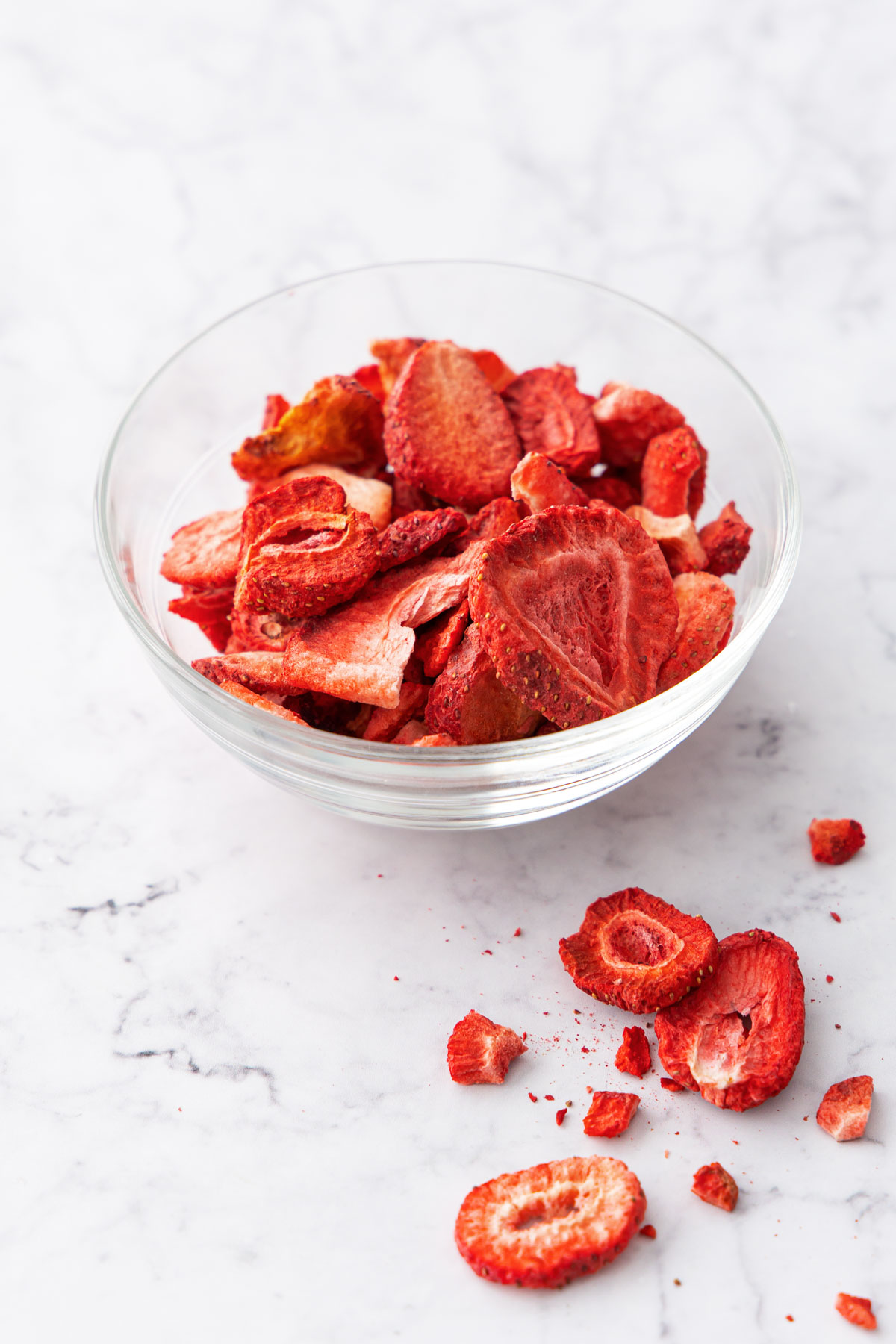 Freeze-dried strawberries in a clear bowl with a few pieces scattered on the background.