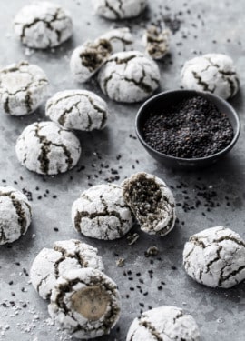 Black Sesame Amaretti Cookies scattered messily on a gray background with a bowl of black sesame seeds.