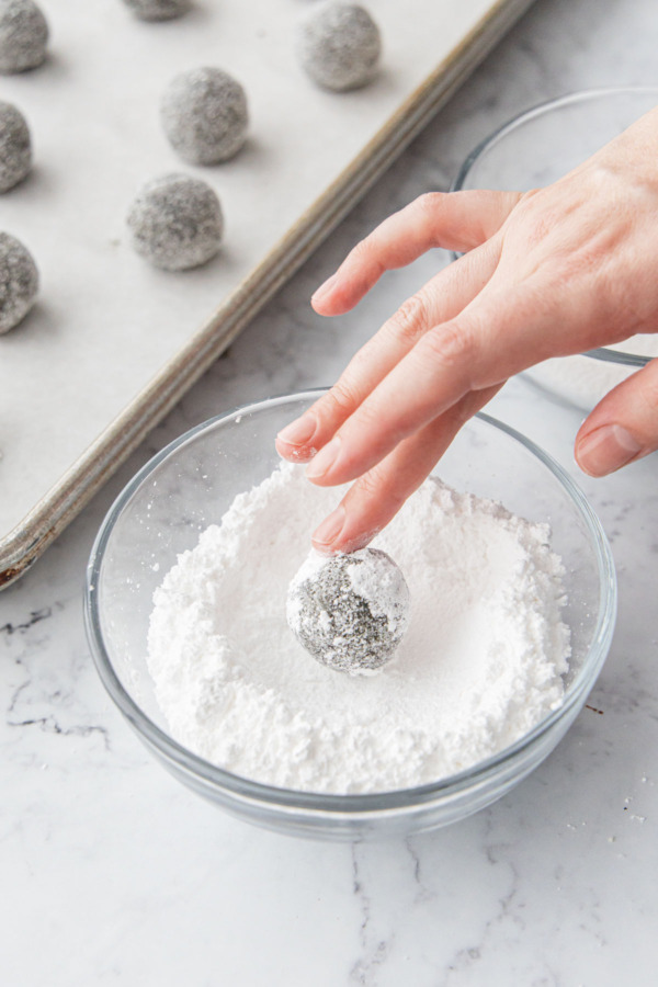 Rolling the dough ball in powdered sugar after coating in granulated sugar first.