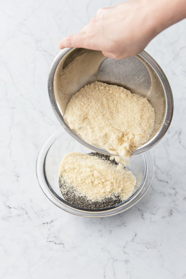 Adding almond flour to a mixing bowl along with ground black sesame bowder.