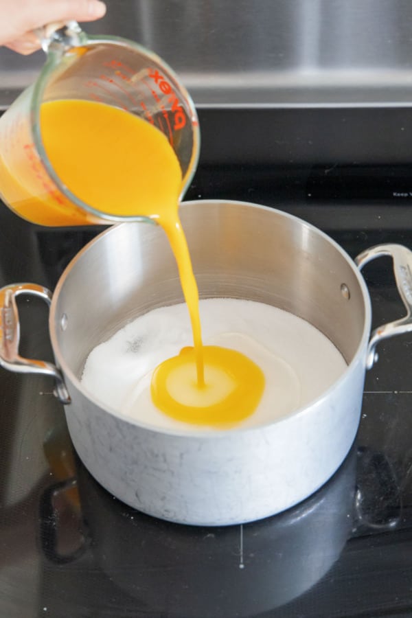 Pouring passionfruit pulp into a saucepan along with sugar and glucose syrup.