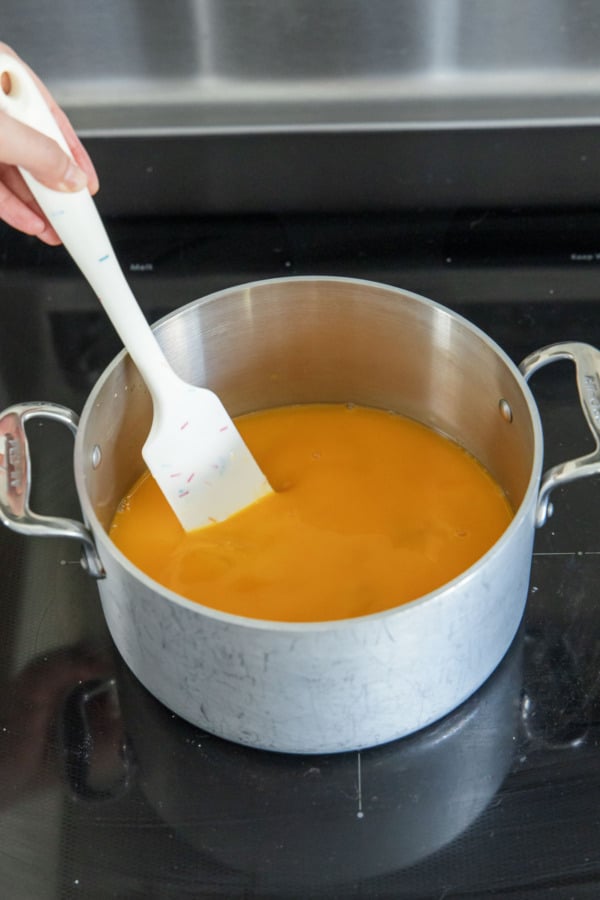 Stirring passionfruit mixture in a saucepan over medium high heat.