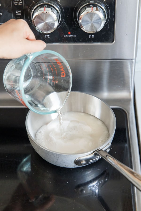 Pouring water into a small saucepan with sugar, pectin, and baking soda causing it to foam.
