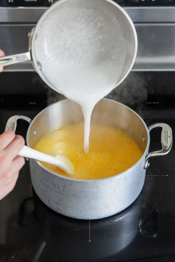 Pouring baking soda-pectin mixture into larger saucepan with passionfruit mixture.