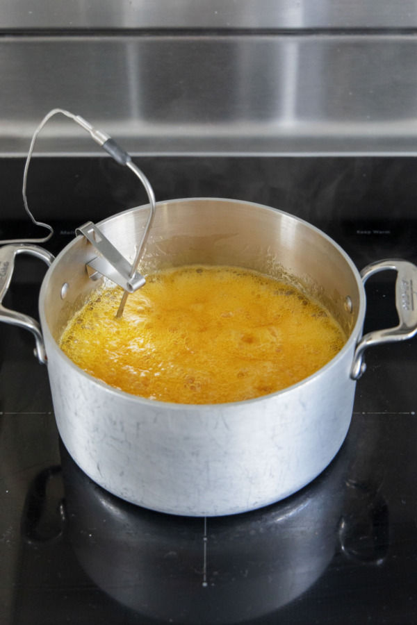 Saucepan full of boiling passionfruit mixture on a stovetop with a probe thermometer attatched.