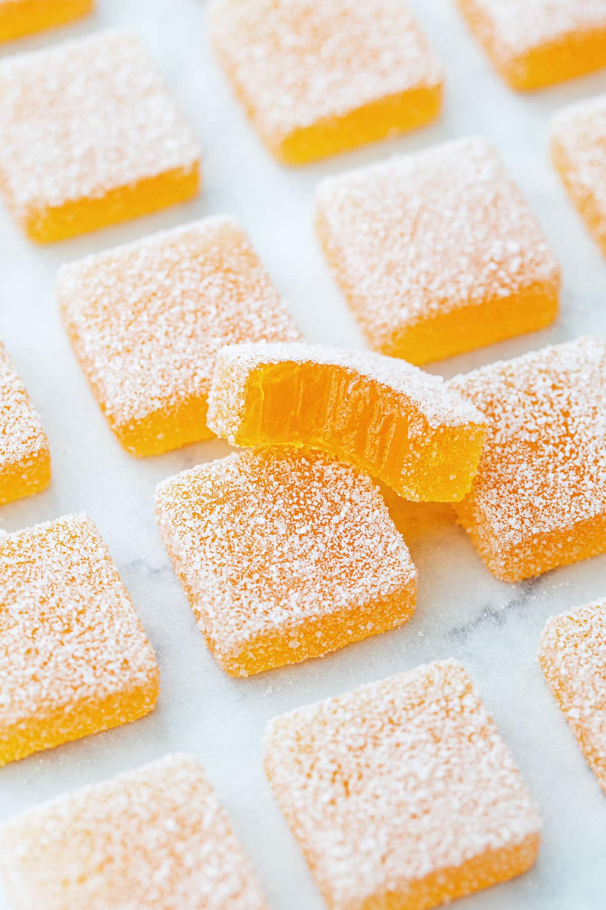Passionfruit Jellies (Pate de Fruit) coated in granulated sugar, a bite out of one piece to show the jammy texture inside.