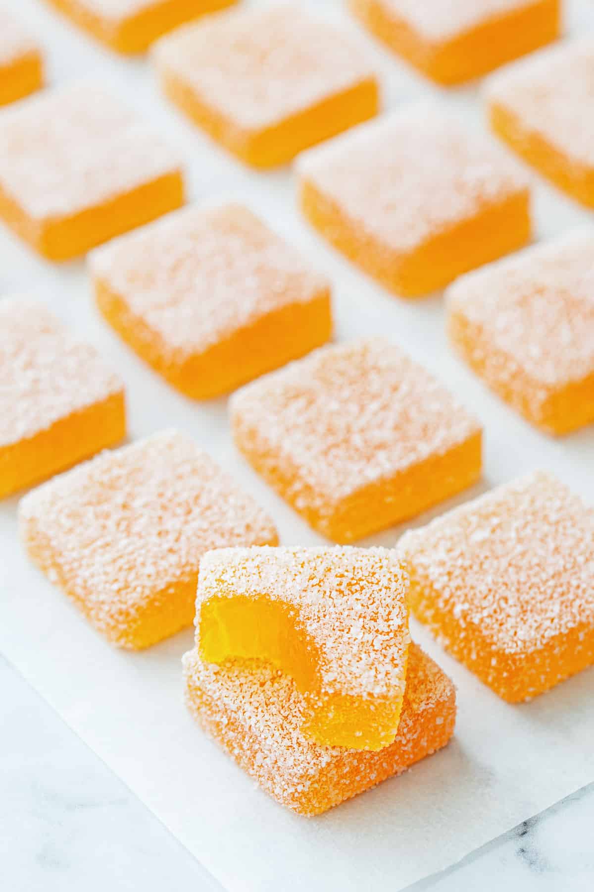 Passionfruit Jellies (Pate de Fruit) coated in granulated sugar, a bite out of one piece to show the jammy texture inside.
