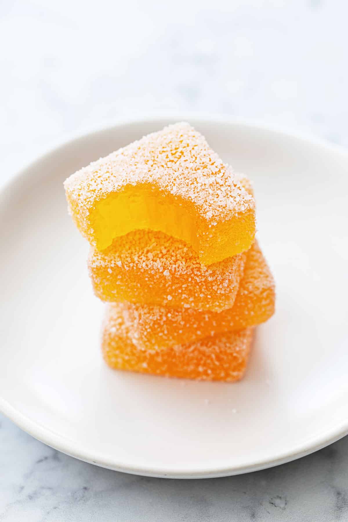 Stack of square pieces of Passionfruit jellies coated in sugar on a small white plate.