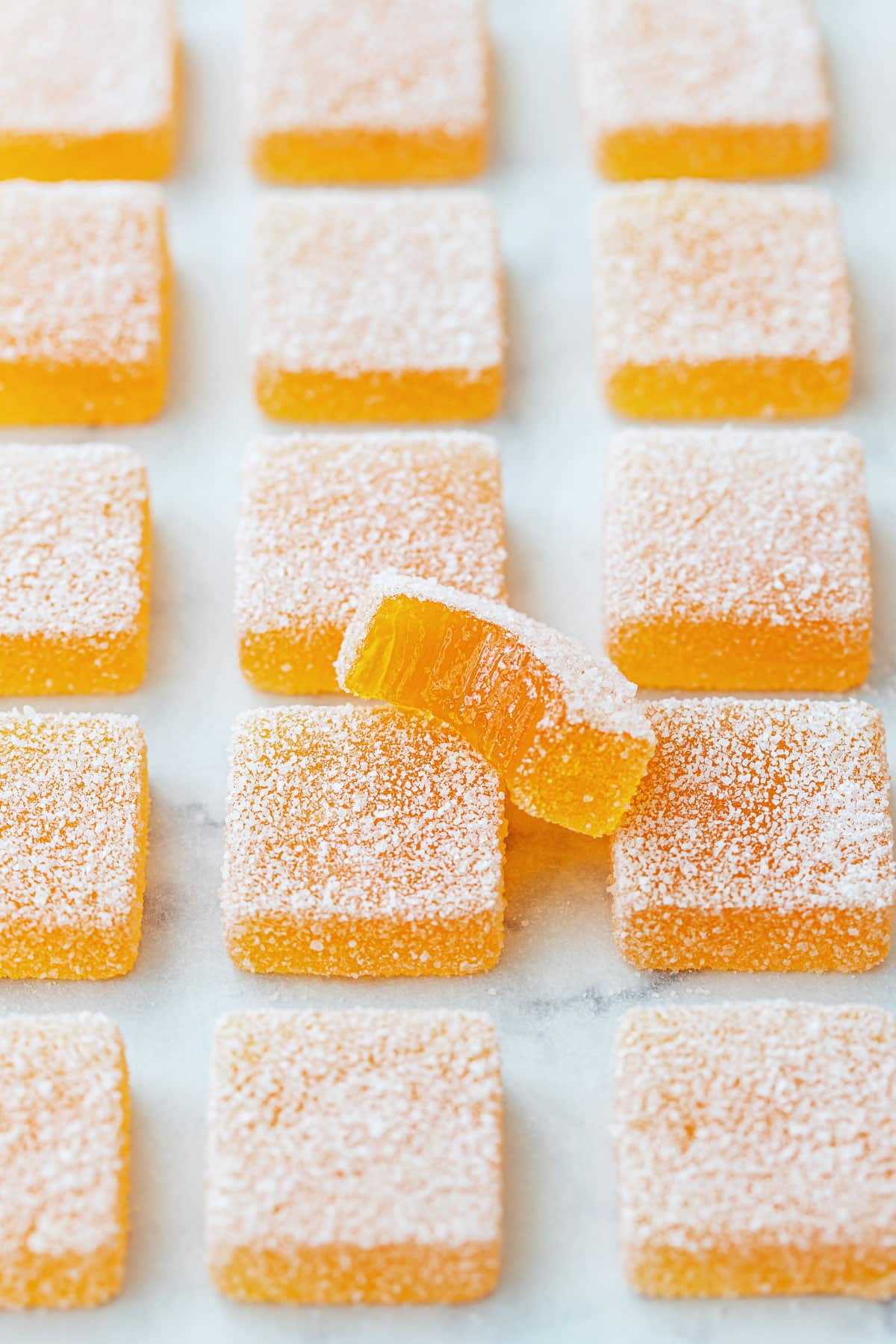 Passionfruit Jellies (Pate de Fruit) coated in granulated sugar, a bite out of one piece to show the jammy texture inside.