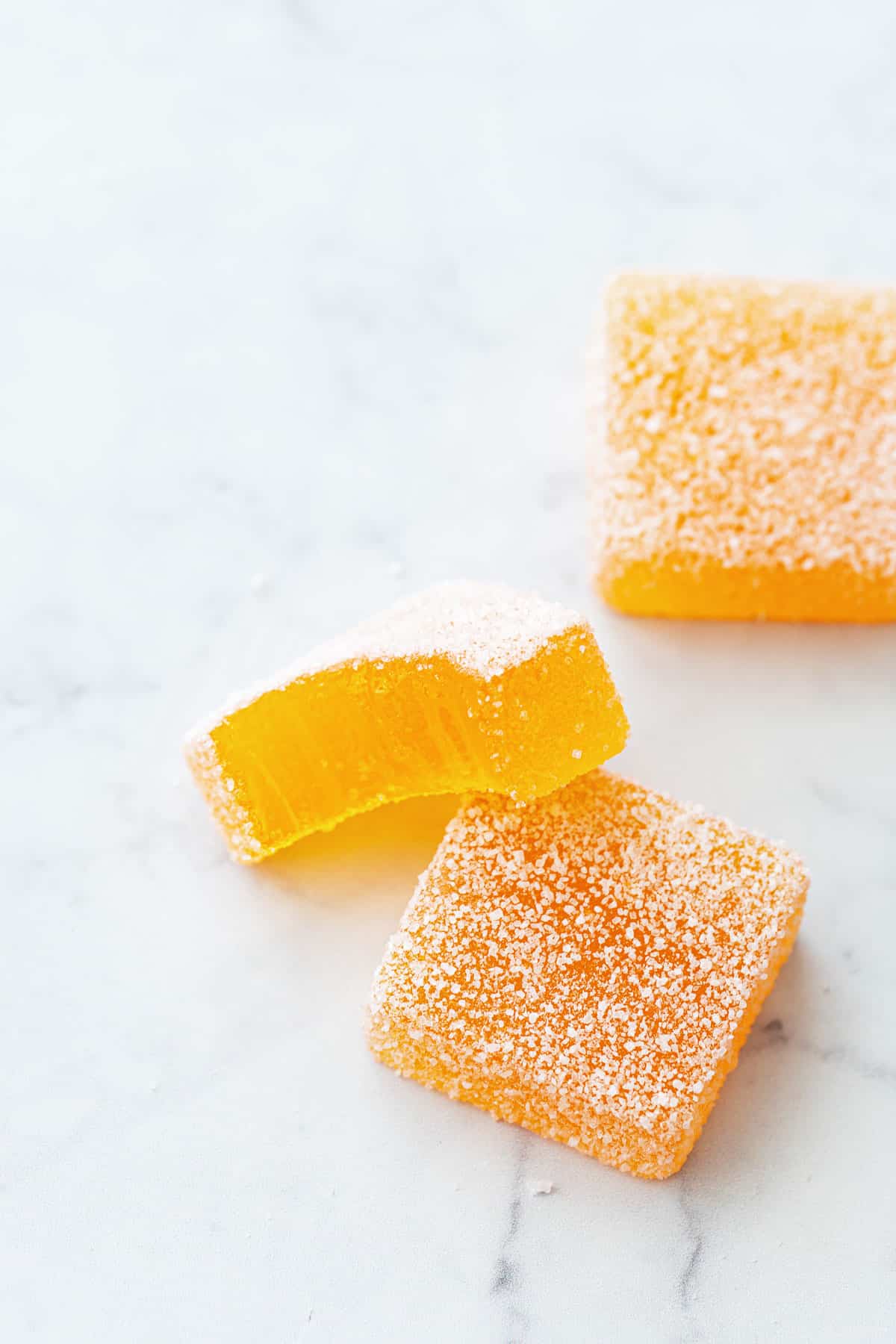 Closeup view of passionfruit pate de fruit jellies on a marble background, a bite taken out of one piece to show the interior texture.