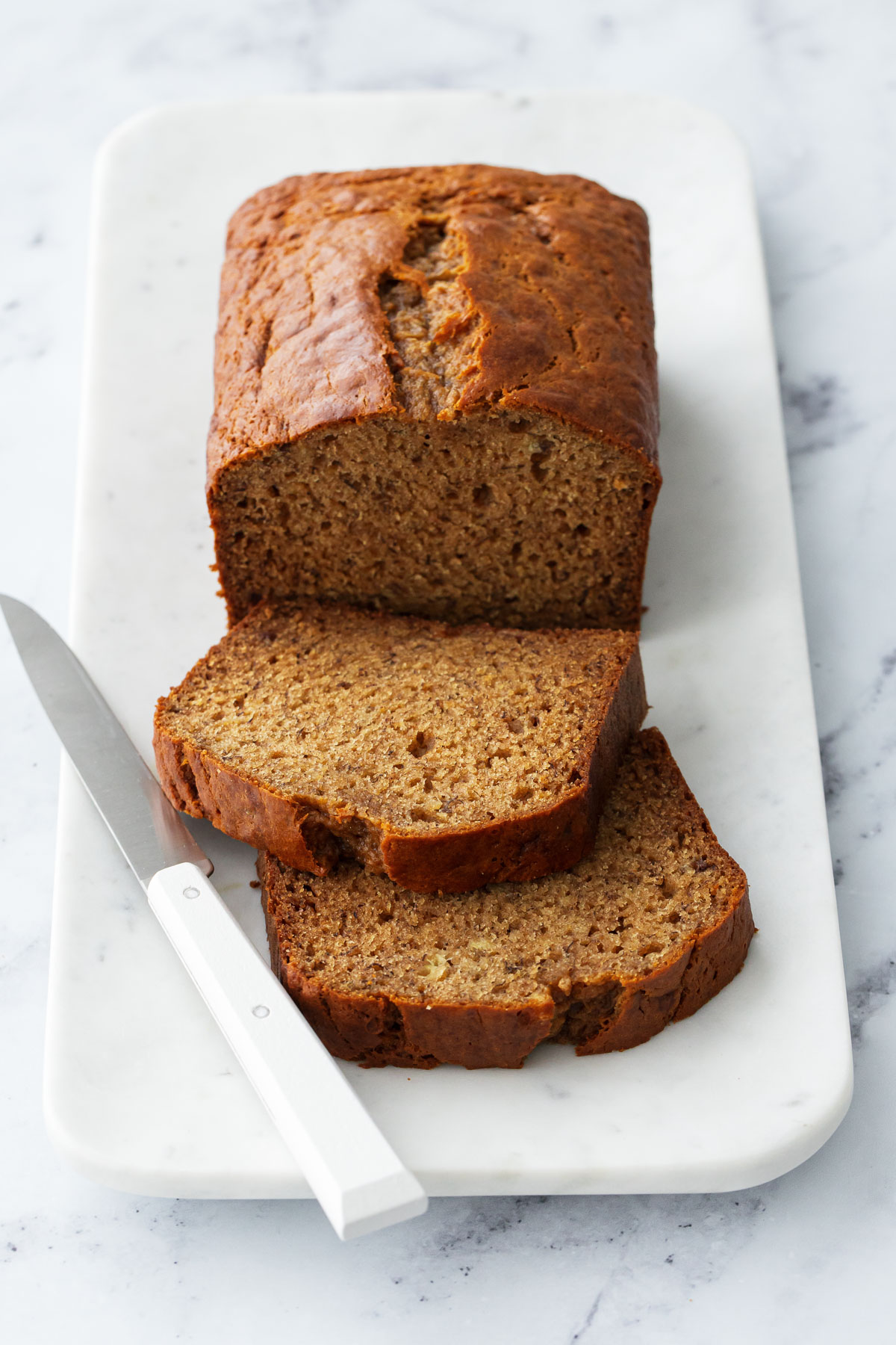 Loaf of Brown Butter Banana Bread on a marble platter, two cut slices laying down to show the interior texture.