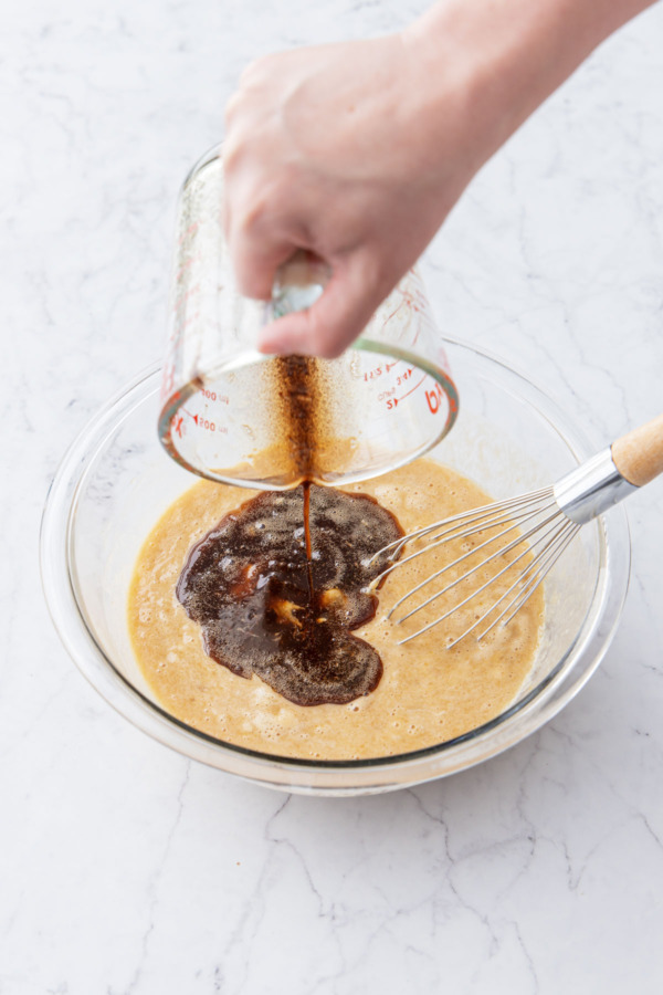 Pouring lukewarm brown butter into mixing bowl with other wet ingredients.