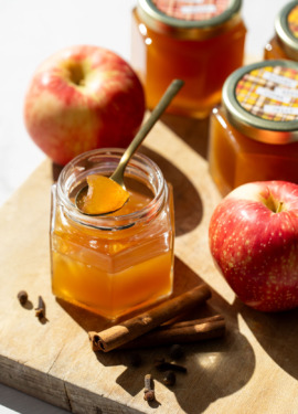 Jar of Spiced Apple Cider Jelly on a wooden board, with a spoonful of jelly resting on top to show the glass-like appearance and texture.