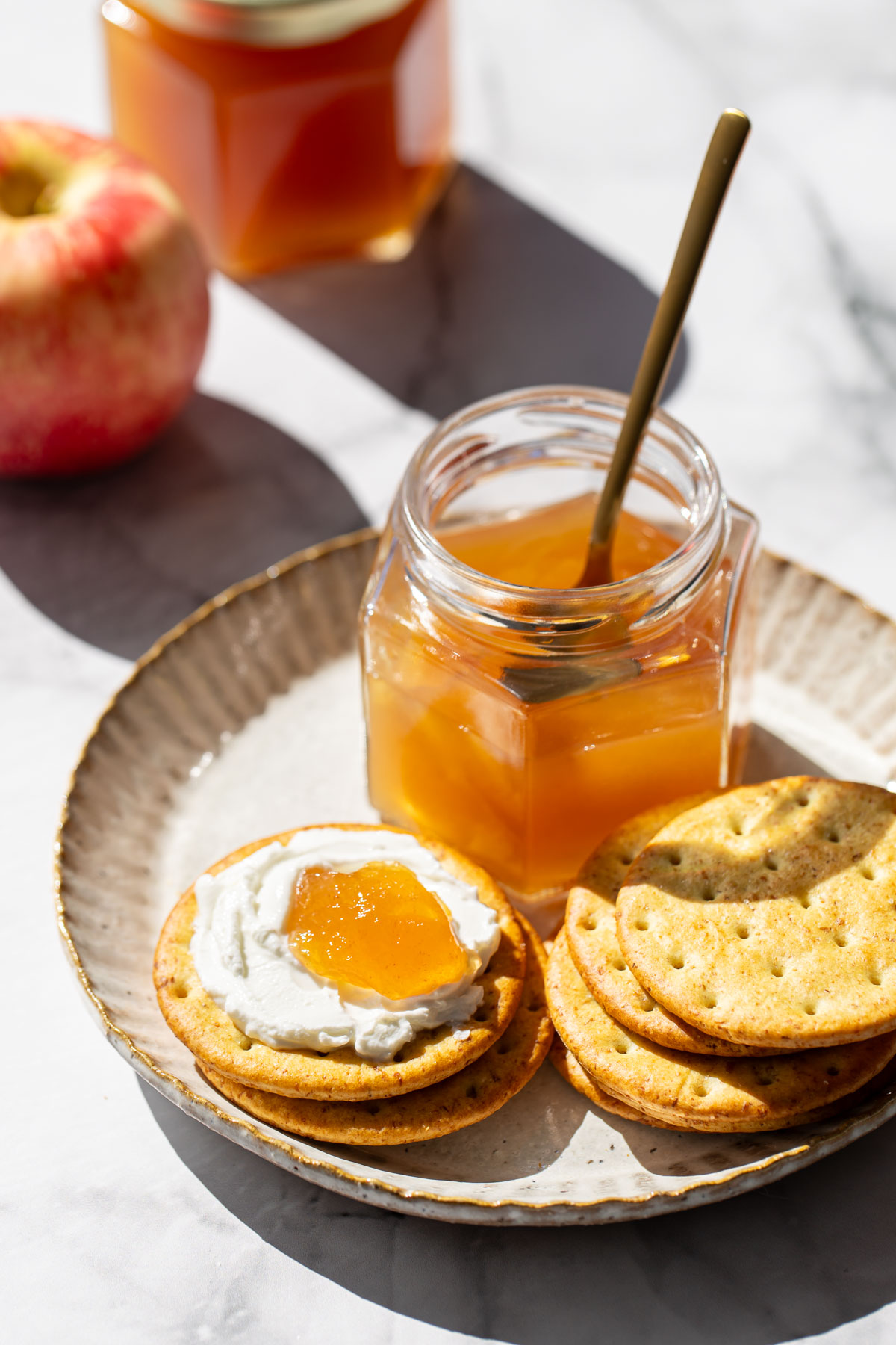 Plate with jar of Spiced Apple Cider Jelly and crackers, one cracker spread with soft cheese and a dollop of apple jelly.