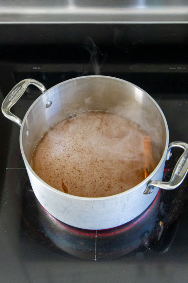 Apple cider simmering on the stovetop with whole spices.