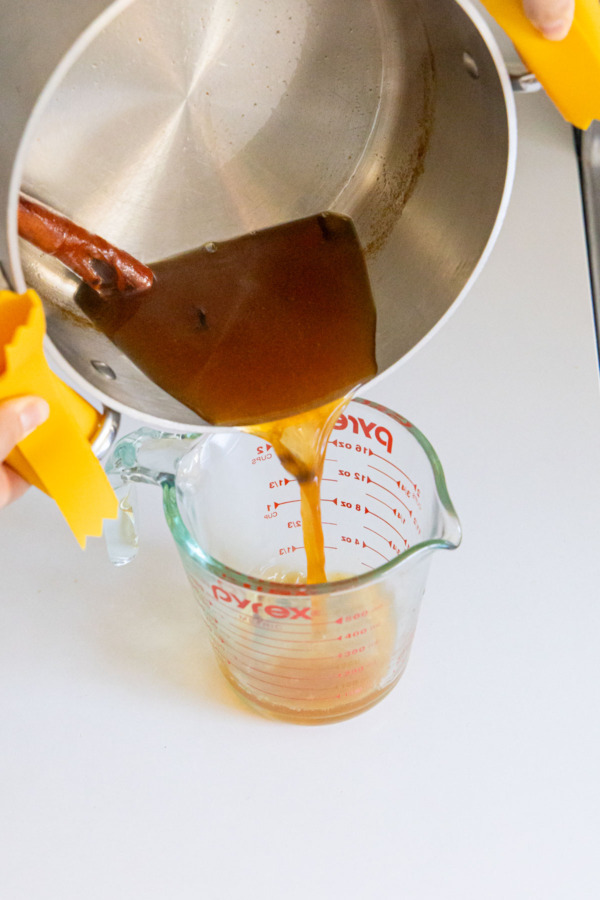 Pouring reduced apple cider into a 2 cup glass measuring cup.
