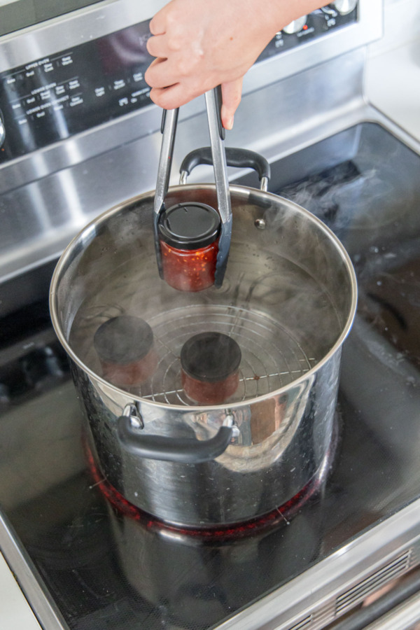 Lowering filled jar into a pot filled with almonst-boiling water.